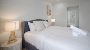 A neatly made bed with white linens, a grey upholstered headboard, and two bedside lamps with woven bases. - 3 Lounges 5 Beds w/ Ducted A/C Modern & Convenient (Rochedale)