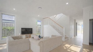 A spacious living room with a large sectional sofa, a flat-screen TV, and a staircase leading to another level. - 3 Lounges 5 Beds w/ Ducted A/C Modern & Convenient (Rochedale)