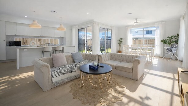 A modern living room with a sofa, a round coffee table, and a kitchen area in the background. - 3 Lounges 5 Beds w/ Ducted A/C Modern & Convenient (Rochedale)