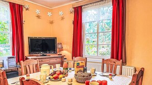 Un comedor con una mesa dispuesta para dos, un televisor y una ventana con cortinas.