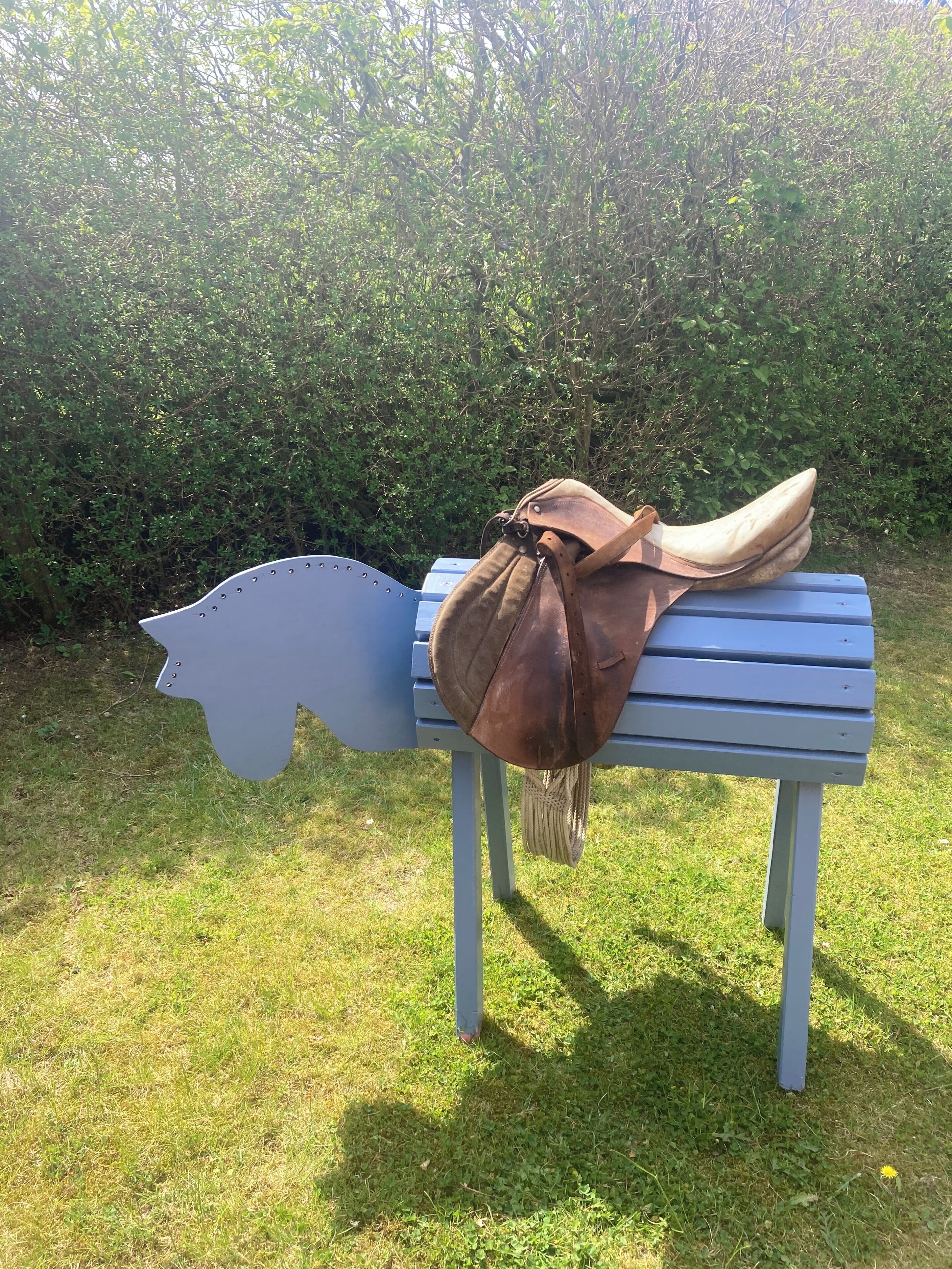 A bench with a brown bag on it, set against a backdrop of green foliage.