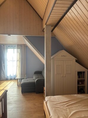 A loft bedroom with a sloped ceiling, a bed, a sofa, and a small white wardrobe labeled 'La Plage'.
