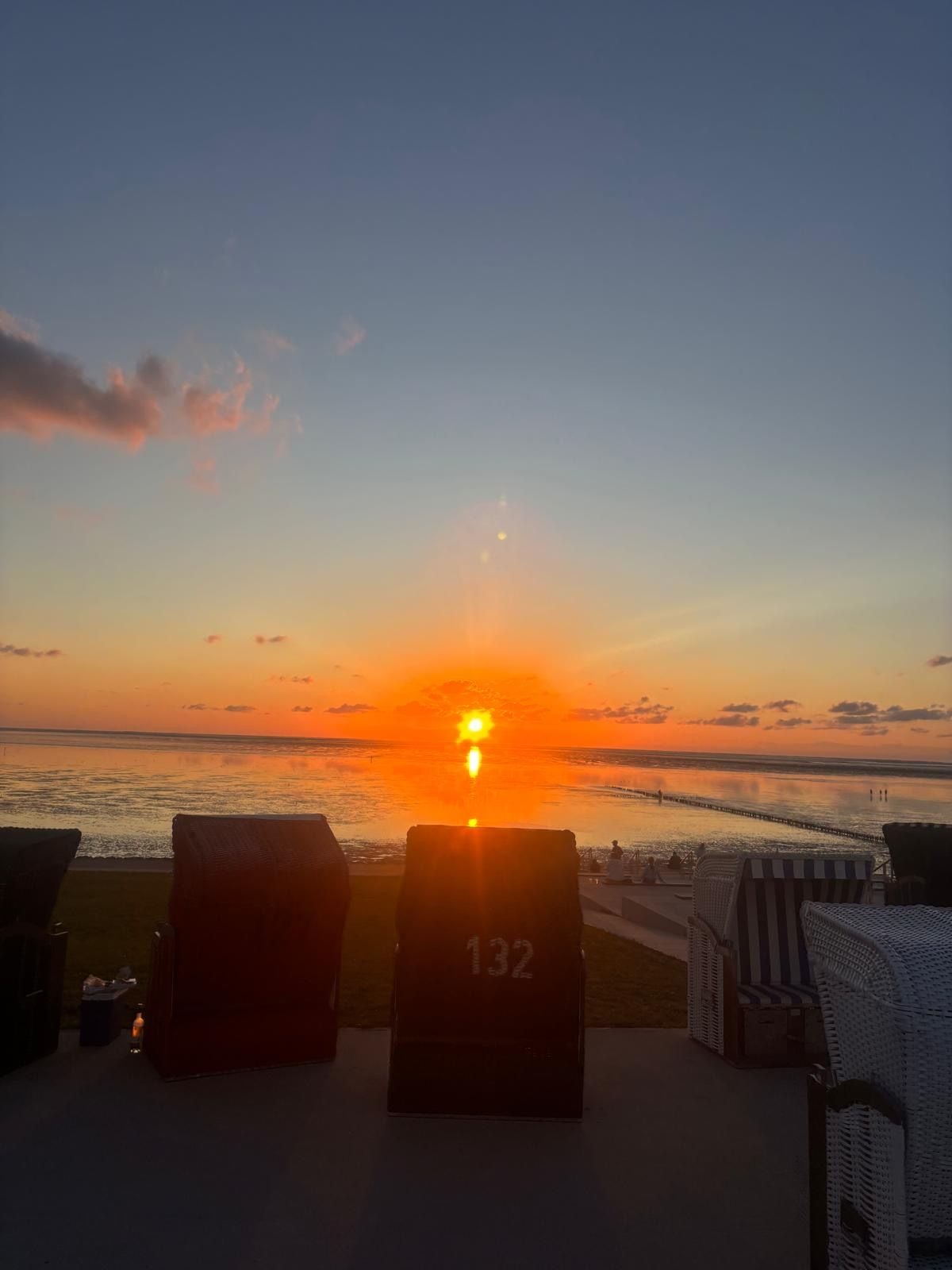 Vista del atardecer desde un área de descanso en la playa, con sillones y un letrero con el número 132.
