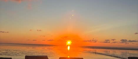 Vista del atardecer desde un área de descanso en la playa, con sillones y un letrero con el número 132.
