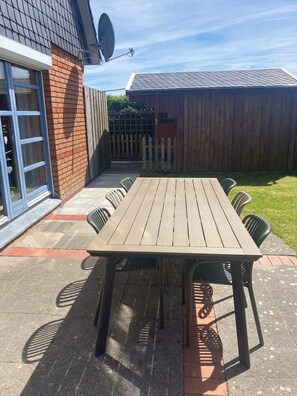 Una mesa de patio de madera con sillas, un muro de ladrillo, una valla de madera y una antena parabólica.