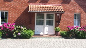 En rød murbygning med markise over en dobbelt dør, omgivet af blomster og potteplanter.