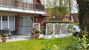 En boligejendom med balkon, patio med udendørs møbler og et hvidt espalierhegn.