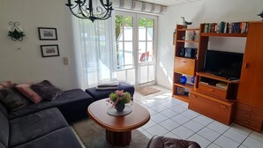 En stue med en sofa, et sofabord med blomster, et tv-skab med bøger og et vindue med gardiner.