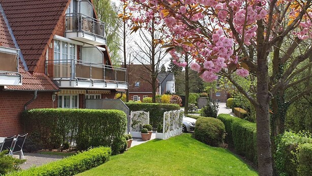 En toetagers bygning med en rød murstensfacade, en balkon og en velplejet have med græsplæne og hække.