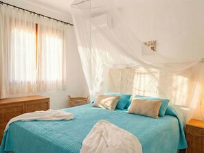 Ein Schlafzimmer mit einem Bett, einem Nachttisch, einem Korbwäscher und einem Himmelbett.