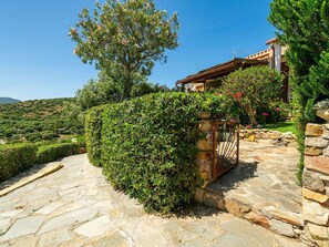 A stone pathway leading to a house with a stone gate, surrounded by lush greenery and a clear blue sky. - Wonderful private villa for 4 guests with WIFI, A/C, TV, patio and pets allowed (Quartu Sant'elena)