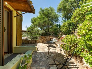 A stone patio with a wooden table and chairs, a stone wall, and a wooden door. - Wonderful private villa for 4 guests with WIFI, A/C, TV, patio and pets allowed (Quartu Sant'elena)
