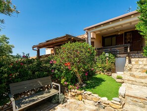 Ein Haus mit einer Steinmauer, einer Holzbank und einem Garten mit verschiedenen Pflanzen und Blumen.