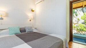 Ein Schlafzimmer mit einem Bett, zwei Wandleuchten, einer Klimaanlage und Blick auf einen Balkon mit Pflanzen.