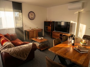 Ein Wohnzimmer mit einer Couch, einem Couchtisch, einem Fernseher und einem Esstisch mit Stühlen.