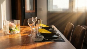 Uma mesa de jantar com copos de vidro transparente, um vaso de flores e um prato preto com comida amarela.