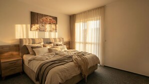 Quarto com cama, mesa de cabeceira, pintura e cortinas leves.