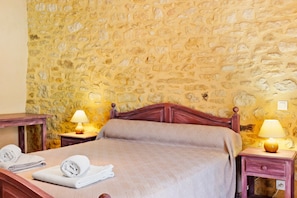 Een kamer met een stenen muur, een houten bed met hoofdeinde, twee nachtkastjes met lampen en een houten nachtkastje met een lamp.