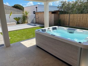 A hot tub in a backyard with a wooden fence, a lawn, and a modern building in the background. - Family home (Saint-Pierre-d'Oléron)