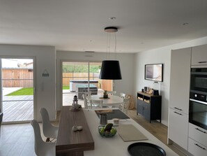 A modern kitchen with a dining area, a large window, and a barbecue in the backyard. - Family home (Saint-Pierre-d'Oléron)