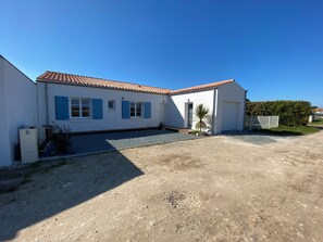 A two-story building with a white exterior and blue shutters, a gravel driveway, and a clear blue sky. - Family home (Saint-Pierre-d'Oléron)