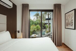 Ein Hotelzimmer mit Bett, Blick auf Pool und Palmen sowie einem gerahmten Kunstwerk an der Wand.