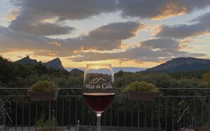 A wine glass with 'Mas de Cala' etched on it, placed on a balcony with a scenic mountain view.