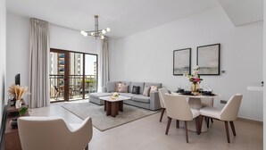A modern living room with a grey sofa, white armchairs, a dining table set for four, and a large window with a view of buildings. - Maison Privee - Relaxed Yas living with Resort-Style Facilities (Abu Dhabi)