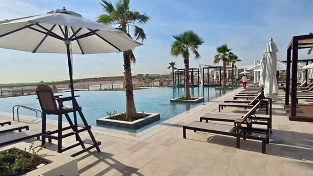 A poolside area with lounge chairs, umbrellas, and palm trees. - Maison Privee - Relaxed Yas living with Resort-Style Facilities (Abu Dhabi)