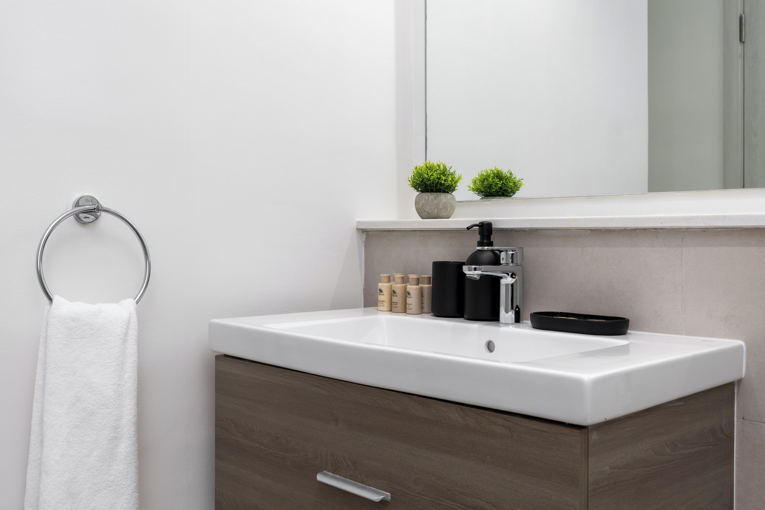 A modern bathroom with a white sink, dark wood cabinet, and a towel ring.
