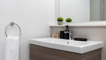 Un baño moderno con lavamanos blanco, mueble de madera oscura y argolla para toallas.