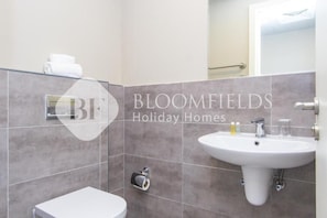 A bathroom with a toilet, a sink, and a towel rack. - Bloomfields Deluxe 1Br Leonardo (Abu Dhabi)