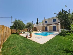 A backyard with a swimming pool, a wooden fence, and a house with a tiled roof.
