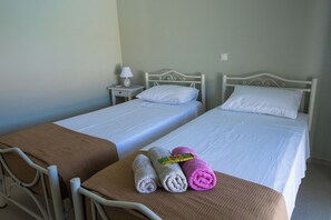 Two single beds with white linens, a brown chair, and three rolled towels on the bed.