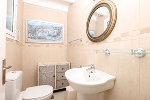 Ein Badezimmer mit Toilette, Waschbecken, Spiegel und einem dekorativen Schrank.