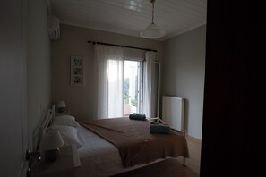 A bedroom with a large bed, a bedside table with a lamp, a window with curtains, and a radiator.