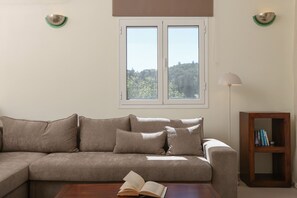 Un salon avec un canapé, une table basse sur laquelle est posé un livre ouvert, une lampe sur pied et une bibliothèque.