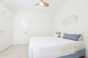 Une chambre à coucher comprenant un lit, un ventilateur de plafond, une armoire et un miroir fixé au mur.
