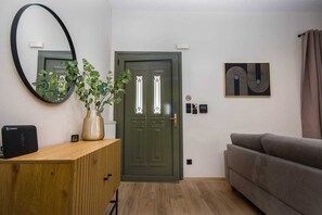 A room with a wooden desk, a green door, a grey sofa, a mirror, and a framed abstract artwork. - Stylish 2BR Base for Exploring Corfu (Corfu)