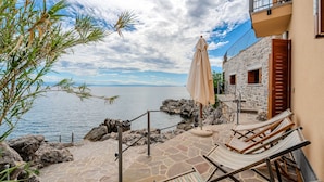 A stone patio with a view of the sea, a lounge chair, and a beach umbrella. - Villa Perfect house beachfront by Villas Guide (Lovran)