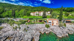 A coastal hotel with multiple buildings, rocky shoreline, and clear turquoise waters. - Villa Perfect house beachfront by Villas Guide (Lovran)