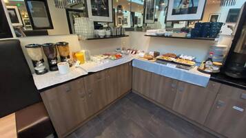 Zona de desayuno tipo buffet con diversas opciones de comida, una estación de café y un cubo de basura.