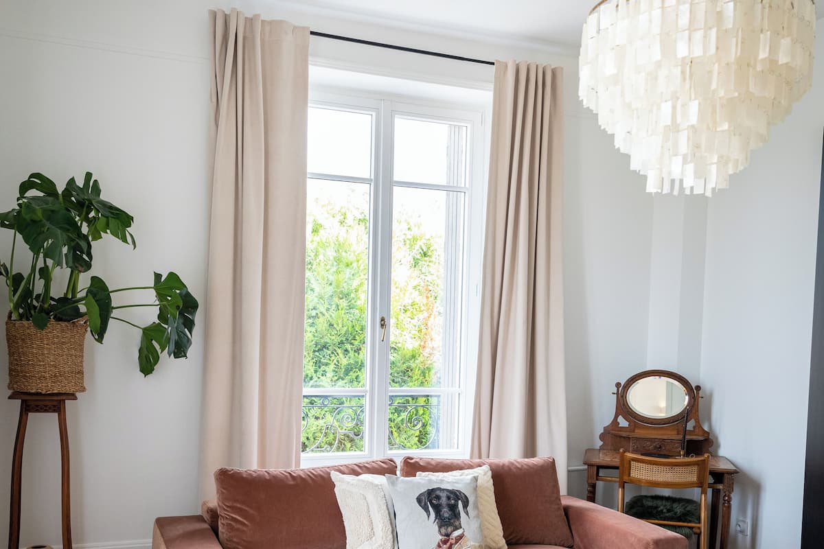 A living room with a sofa, two coffee tables, a chandelier, a potted plant, and a window with curtains.