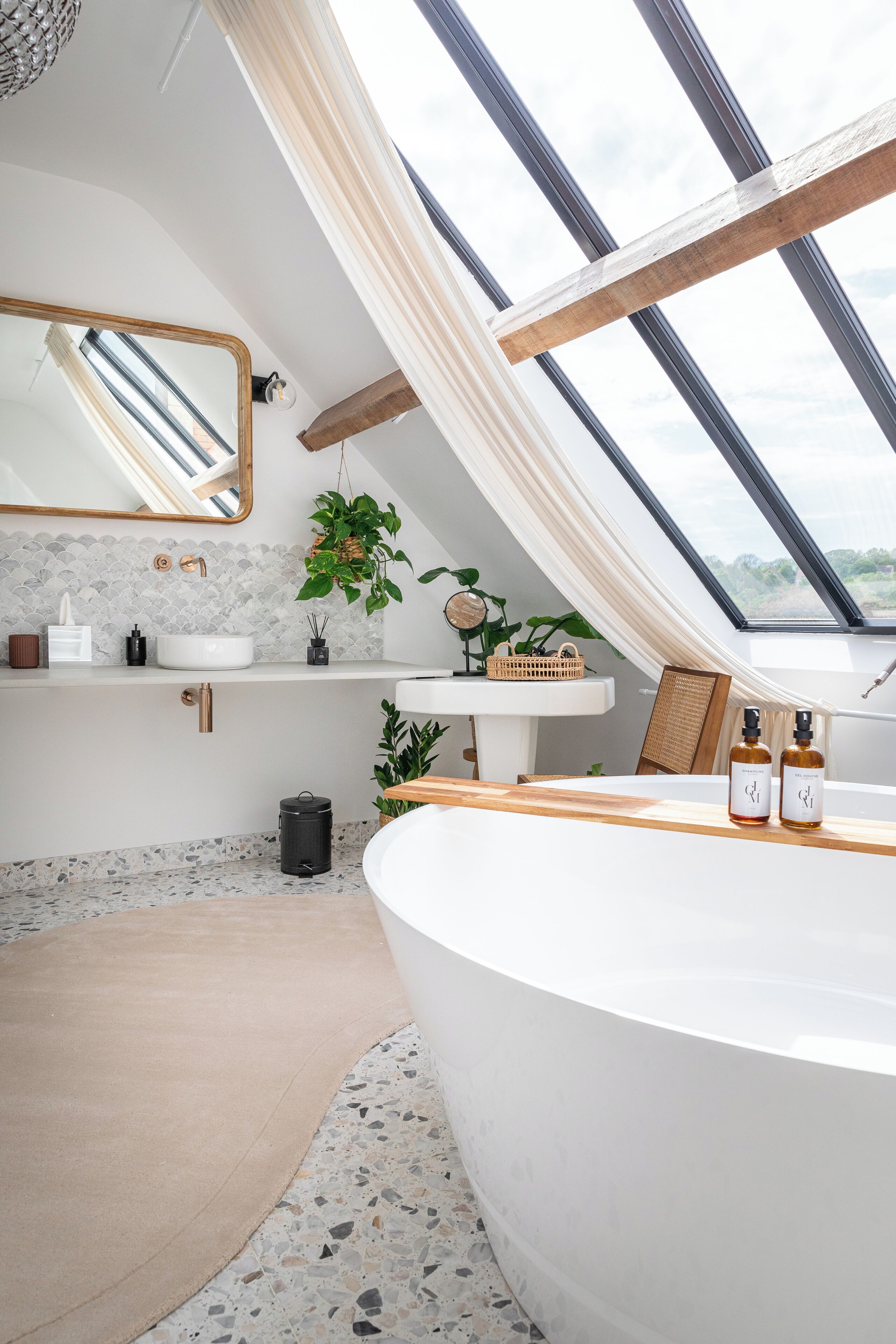 A modern bathroom with a skylight, a freestanding bathtub, a vanity with a mirror, and a plant.