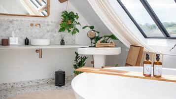 A modern bathroom with a skylight, a freestanding bathtub, a vanity with a mirror, and a plant.