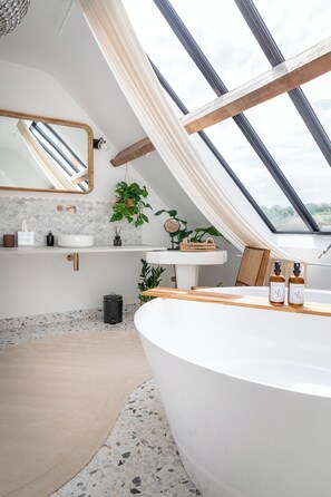 A modern bathroom with a skylight, a freestanding bathtub, a vanity with a mirror, and a plant. - La Grande Maison LGM  (Lesches)
