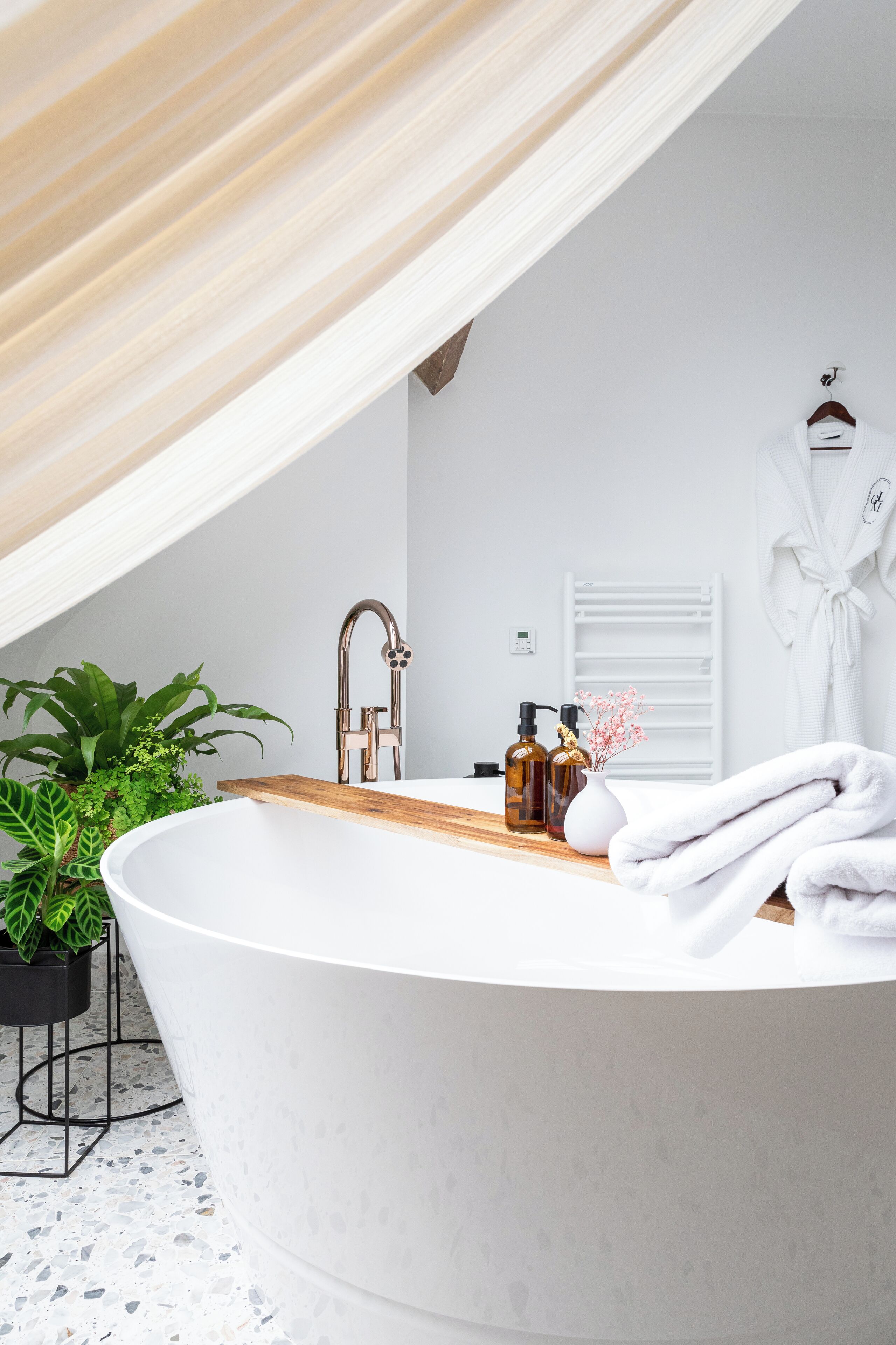 A modern bathroom with a freestanding bathtub, a wooden vanity, a white towel, and a potted plant.