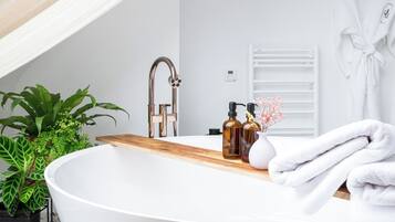 A modern bathroom with a freestanding bathtub, a wooden vanity, a white towel, and a potted plant.