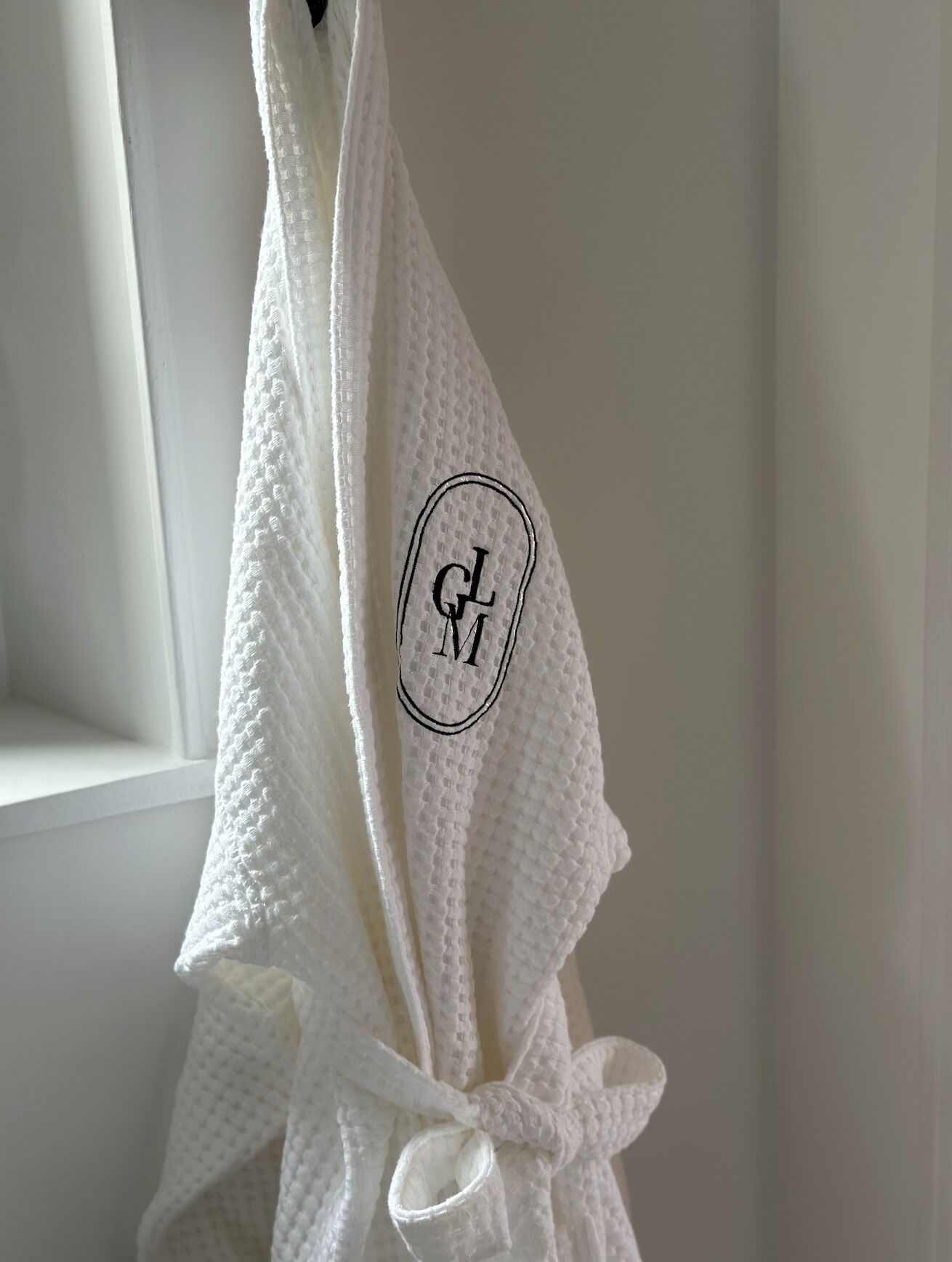 A white robe with a monogrammed logo hanging on a white wall.