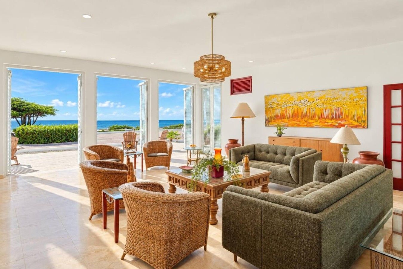 Uma sala de estar ampla com vista para o mar, móveis de vime e um quadro grande na parede.